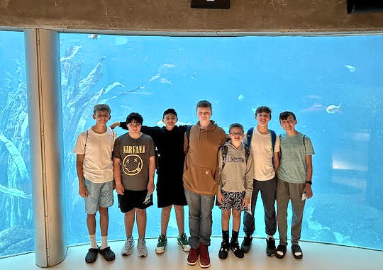 Group of male middle school students standing in front of an aquatic exhibit and smiling for a group photo.