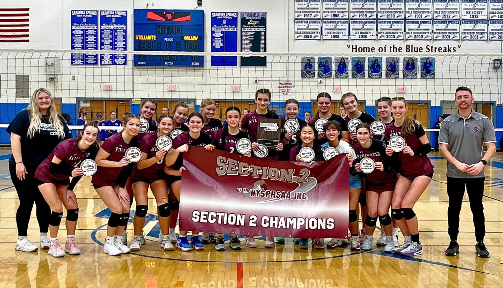 Stillwater girls varsity volleyball team poses in a gymnasium holding a "Section 2 Champions" banner and individual awards.