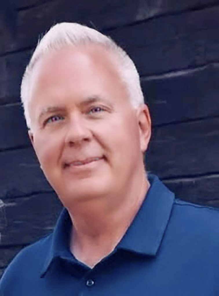 Man with short white hair wearing a blue polo shirt smiling at the camera.