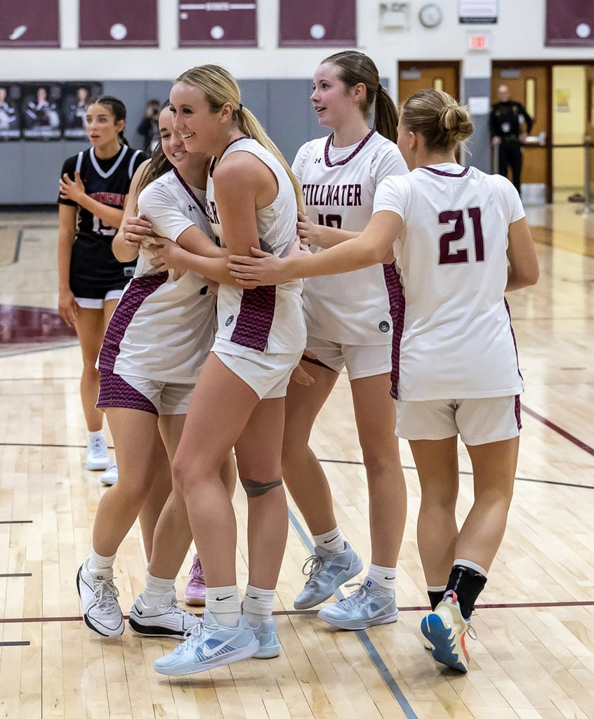 Three teammates surround one player and hug her on the basketball court.