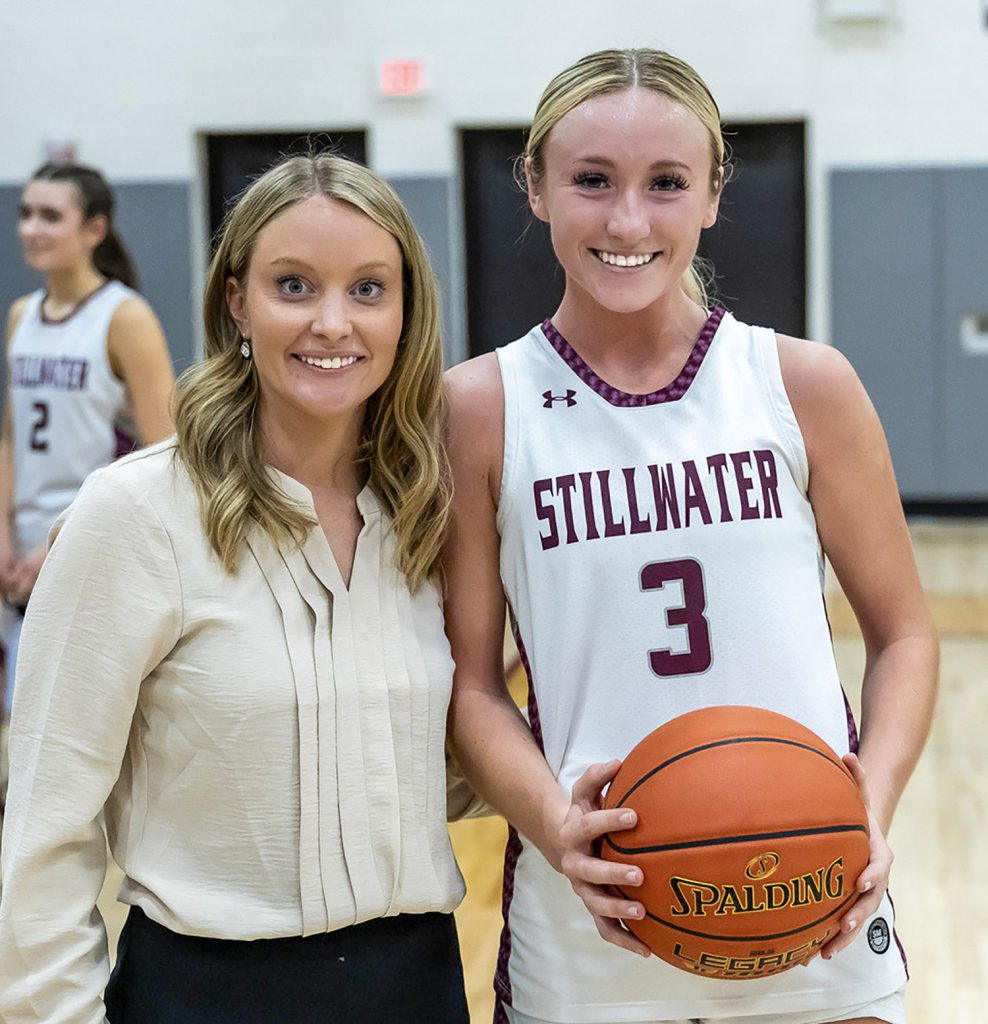 Coach smiling with one of her players, who's holding a basketball.